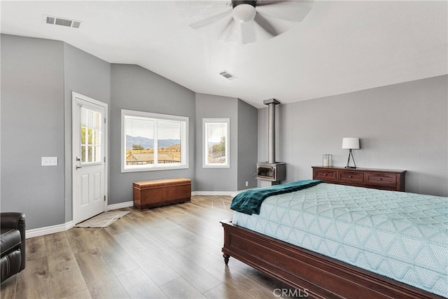 bedroom featuring ceiling fan, lofted ceiling, light hardwood / wood-style floors, and a wood stove