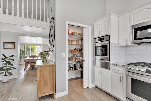 kitchen with stainless steel appliances, light hardwood / wood-style floors, tasteful backsplash, and white cabinetry