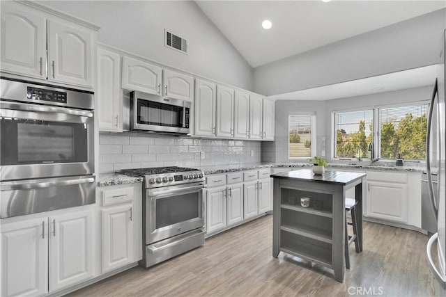 kitchen with light stone countertops, decorative backsplash, white cabinets, light hardwood / wood-style flooring, and appliances with stainless steel finishes