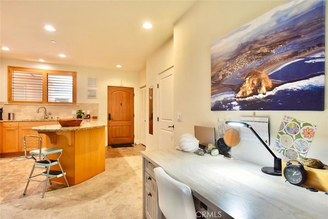 kitchen with light stone counters, a sink, backsplash, recessed lighting, and a breakfast bar area