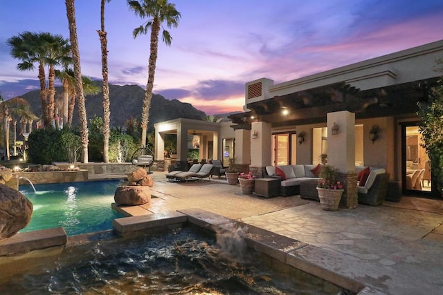 pool at dusk featuring pool water feature, a mountain view, an outdoor living space, and a patio