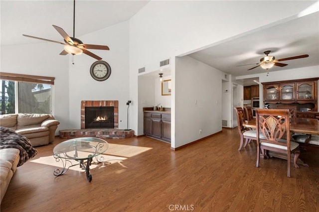 living room with ceiling fan, high vaulted ceiling, dark hardwood / wood-style floors, and a brick fireplace