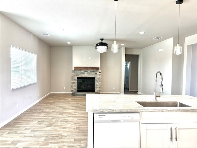 kitchen with white dishwasher, sink, white cabinets, light hardwood / wood-style floors, and hanging light fixtures