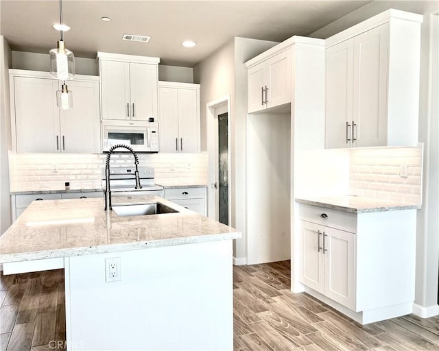 kitchen with tasteful backsplash, a center island with sink, white cabinets, and light hardwood / wood-style floors