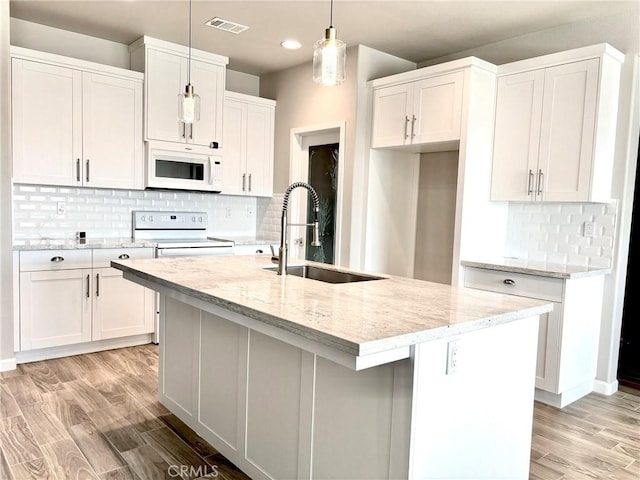 kitchen with a kitchen island with sink, sink, hanging light fixtures, and white appliances