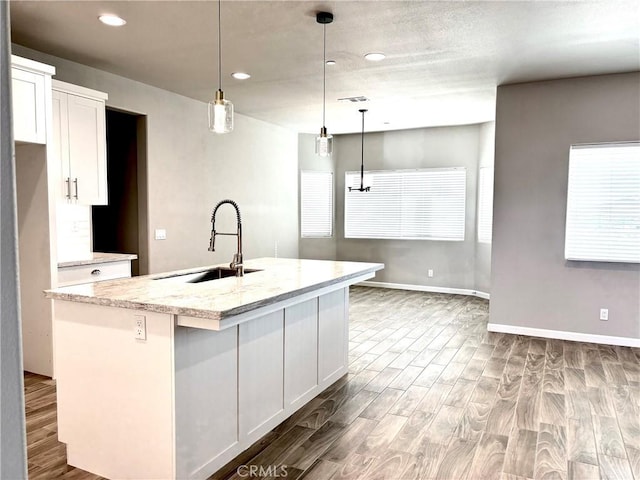 kitchen featuring white cabinetry, sink, light stone counters, an island with sink, and pendant lighting