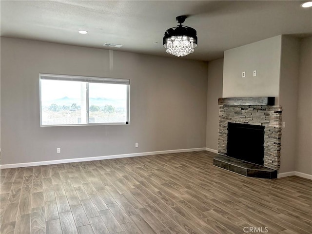 unfurnished living room with a stone fireplace, hardwood / wood-style floors, and an inviting chandelier