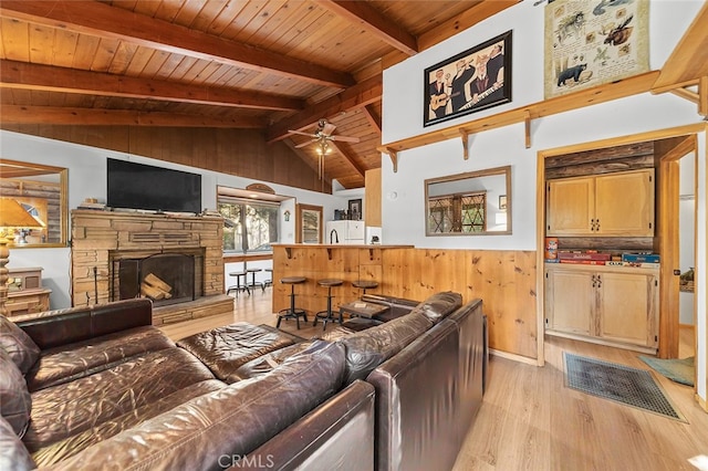 living room with wood walls, light hardwood / wood-style flooring, wood ceiling, a stone fireplace, and vaulted ceiling with beams