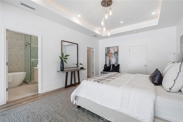 bedroom featuring a raised ceiling, ensuite bathroom, and hardwood / wood-style floors