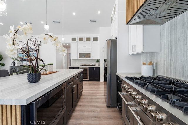 kitchen with a center island, appliances with stainless steel finishes, range hood, light hardwood / wood-style floors, and white cabinetry