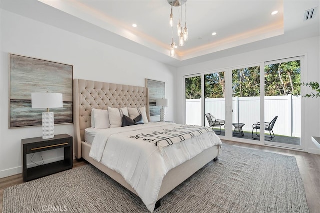 bedroom with a raised ceiling, access to exterior, and hardwood / wood-style flooring