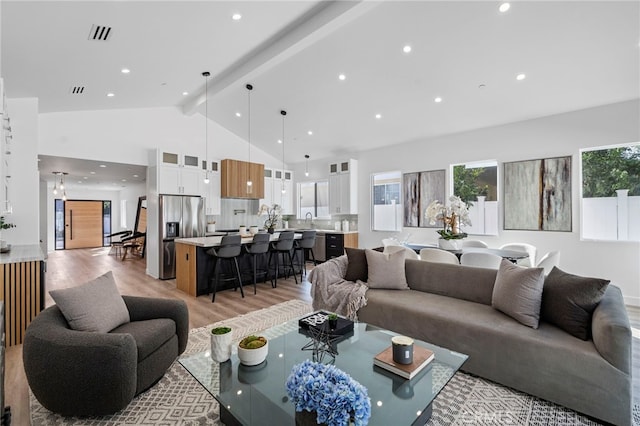 living room with light hardwood / wood-style flooring, beamed ceiling, high vaulted ceiling, and sink