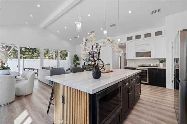 kitchen with tasteful backsplash, a breakfast bar, a kitchen island with sink, light hardwood / wood-style flooring, and white cabinets