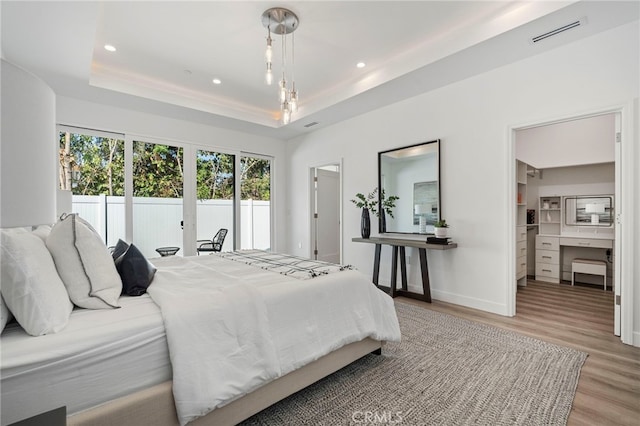 bedroom with access to outside, light hardwood / wood-style floors, and a tray ceiling