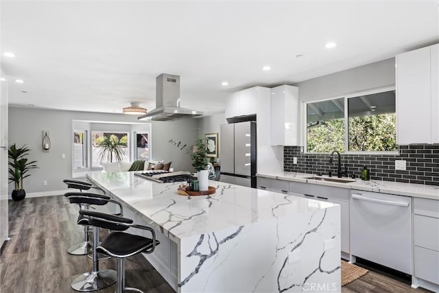 kitchen featuring sink, appliances with stainless steel finishes, range hood, a kitchen island, and white cabinetry