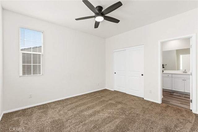 unfurnished bedroom with dark colored carpet, a closet, ensuite bath, sink, and ceiling fan