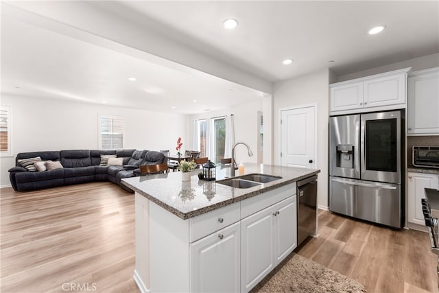 kitchen featuring dishwasher, a kitchen island with sink, sink, stainless steel fridge, and white cabinets