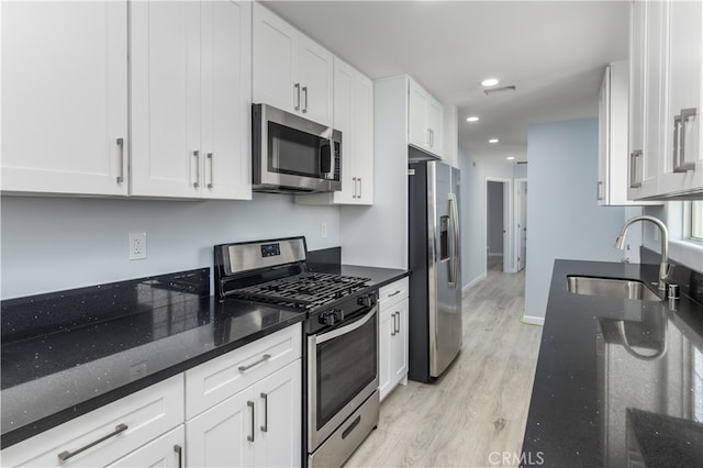 kitchen with white cabinets, sink, appliances with stainless steel finishes, dark stone countertops, and light wood-type flooring