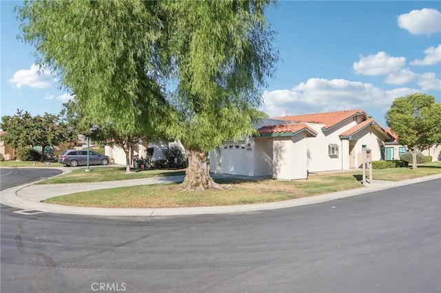 view of front of house with stucco siding, driveway, a front yard, an attached garage, and a tiled roof