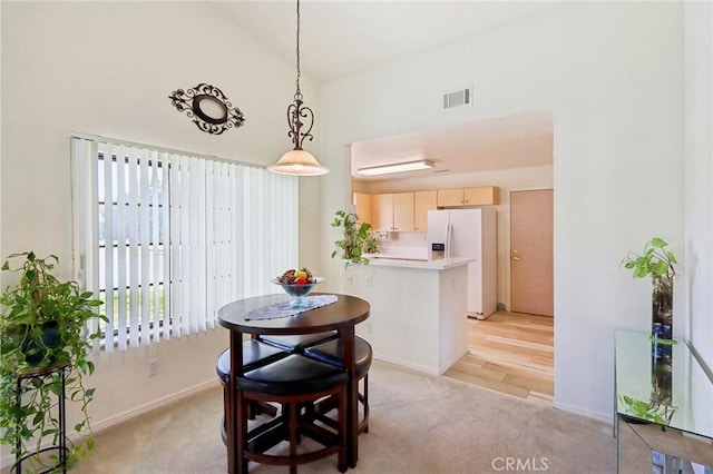 dining room featuring visible vents, light carpet, high vaulted ceiling, and baseboards