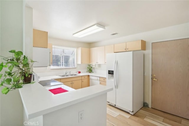 kitchen with light brown cabinets, a sink, white appliances, a peninsula, and light countertops