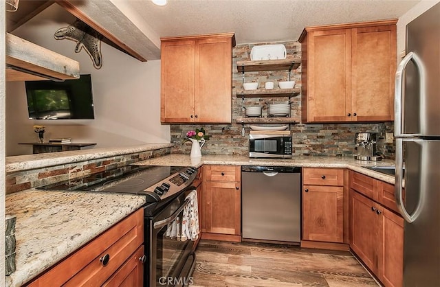 kitchen featuring tasteful backsplash, light stone counters, appliances with stainless steel finishes, and light hardwood / wood-style flooring