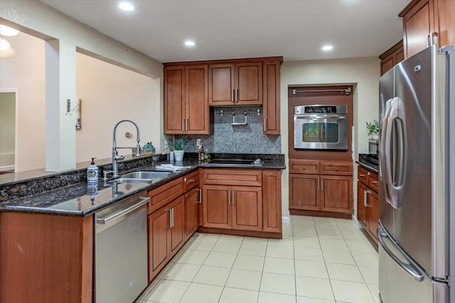 kitchen with appliances with stainless steel finishes, dark stone counters, sink, backsplash, and kitchen peninsula