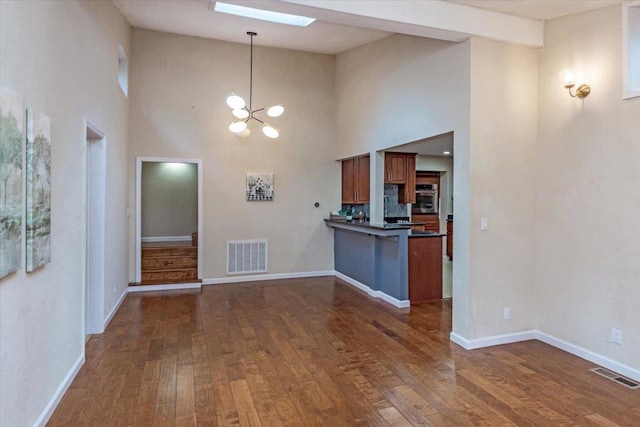 kitchen with a towering ceiling, decorative light fixtures, dark hardwood / wood-style flooring, kitchen peninsula, and a notable chandelier