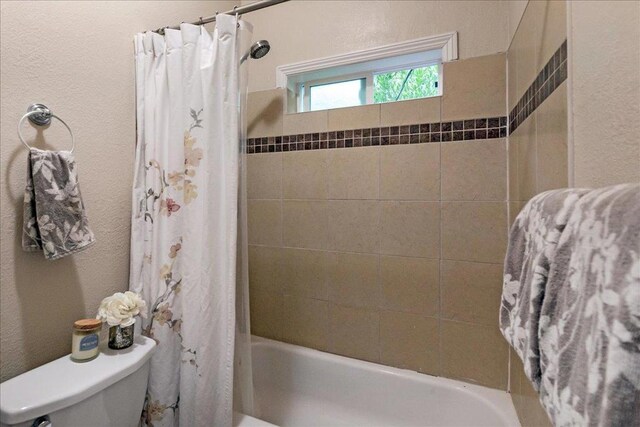 bathroom featuring toilet and shower / bath combination with curtain