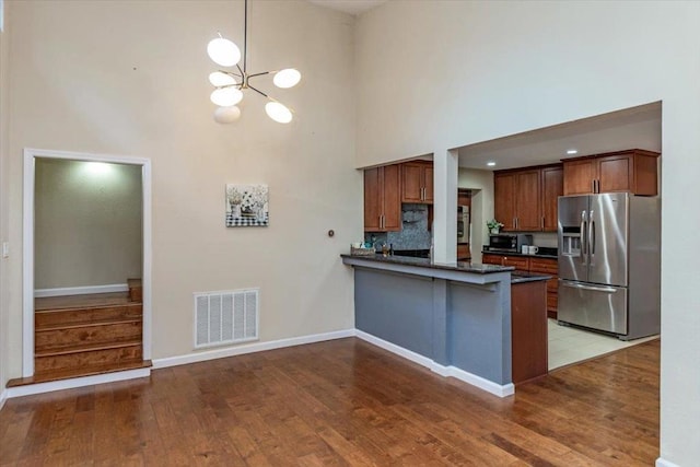 kitchen featuring backsplash, kitchen peninsula, stainless steel refrigerator with ice dispenser, an inviting chandelier, and a high ceiling