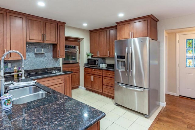 kitchen featuring stainless steel appliances, backsplash, dark stone counters, and sink