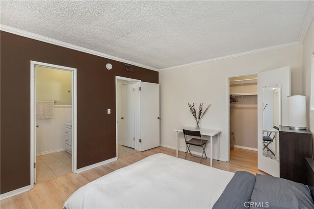 bedroom featuring crown molding, a walk in closet, a closet, light wood-type flooring, and ensuite bath