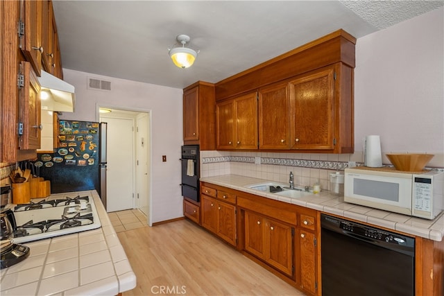 kitchen with sink, white appliances, light hardwood / wood-style flooring, backsplash, and tile countertops