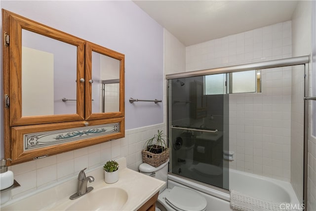 full bathroom featuring bath / shower combo with glass door, tile walls, toilet, and vanity