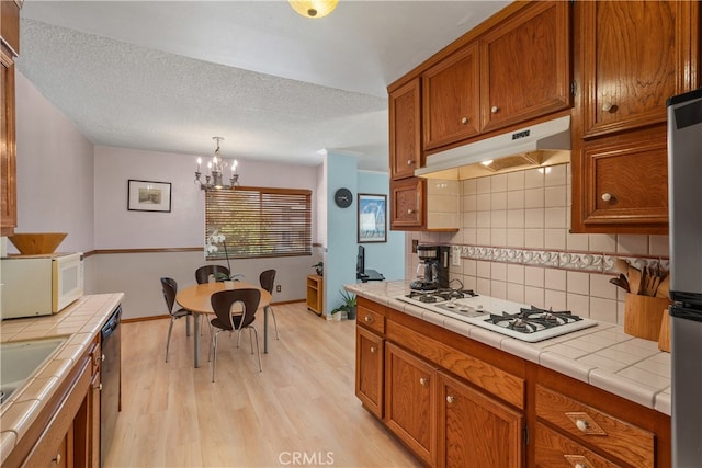 kitchen with stainless steel appliances, an inviting chandelier, light hardwood / wood-style flooring, decorative light fixtures, and tile countertops