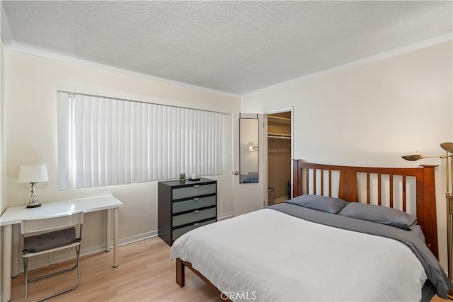 bedroom with light wood-type flooring, a closet, a walk in closet, ornamental molding, and a textured ceiling