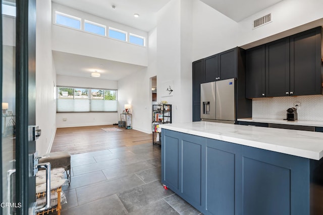 kitchen with a high ceiling, dark wood-type flooring, decorative backsplash, light stone countertops, and stainless steel refrigerator with ice dispenser