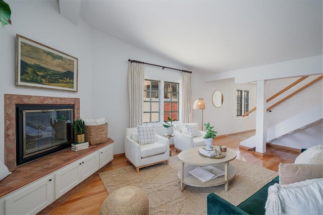 living room with a fireplace, vaulted ceiling, and light wood-type flooring