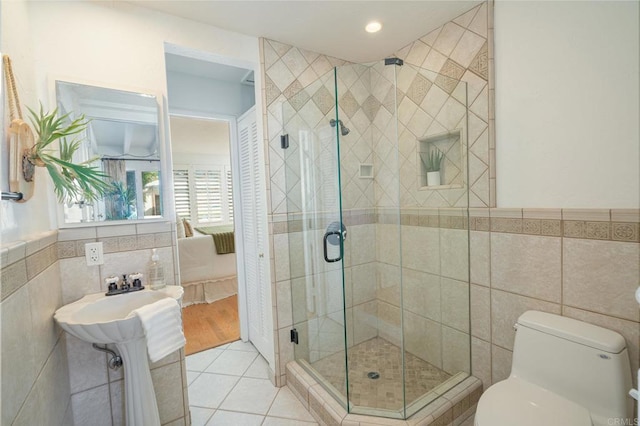 bathroom featuring tile patterned floors, toilet, tile walls, and a shower with shower door