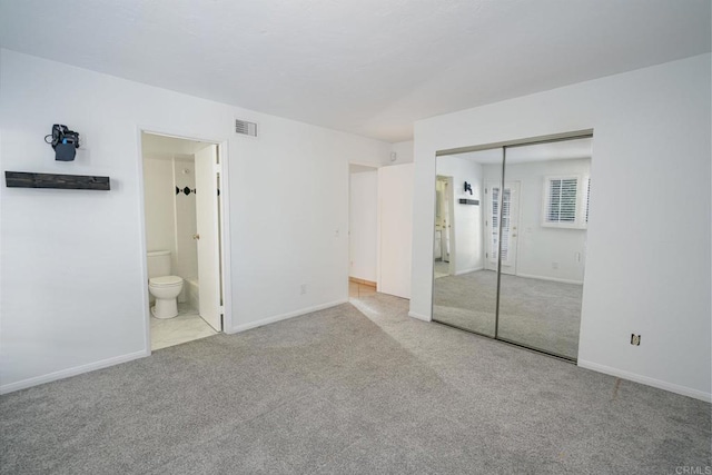 unfurnished bedroom featuring light carpet, ensuite bath, and a closet