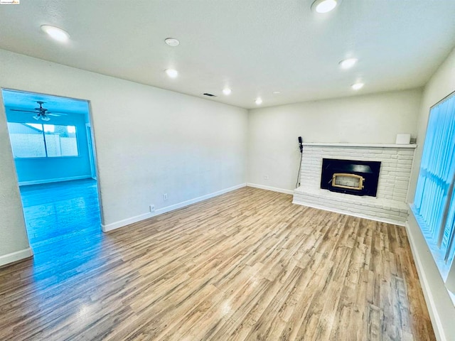 unfurnished living room with light wood-type flooring, a healthy amount of sunlight, and a brick fireplace