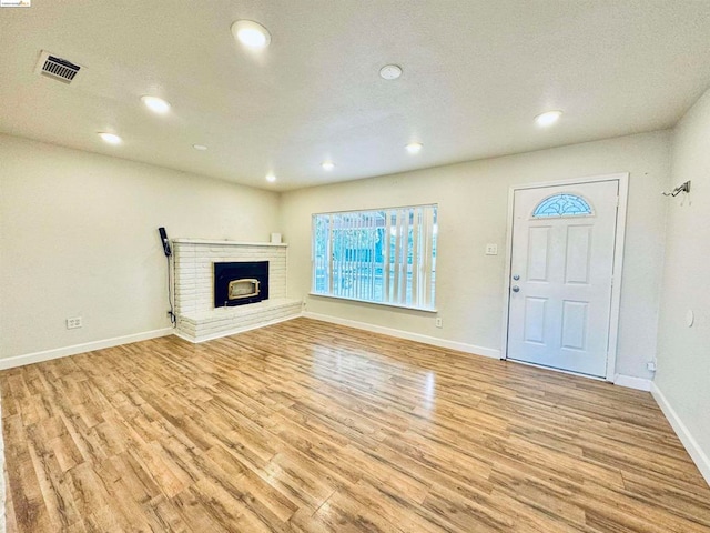 unfurnished living room with a brick fireplace, light hardwood / wood-style floors, and a textured ceiling