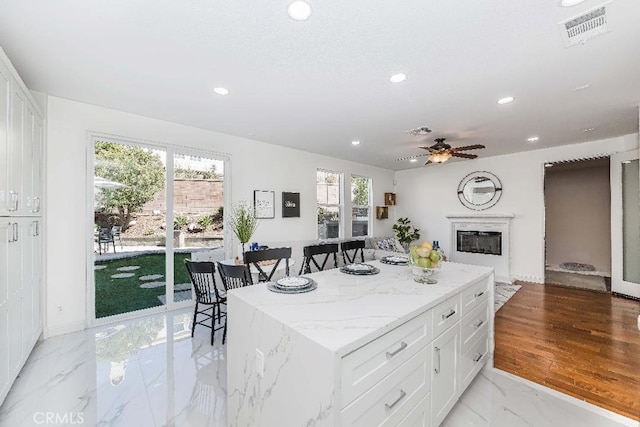 kitchen featuring white cabinets, ceiling fan, a center island, and light stone countertops