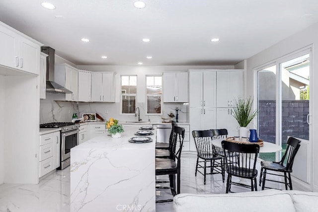 kitchen featuring gas range, white cabinetry, a center island, sink, and wall chimney exhaust hood