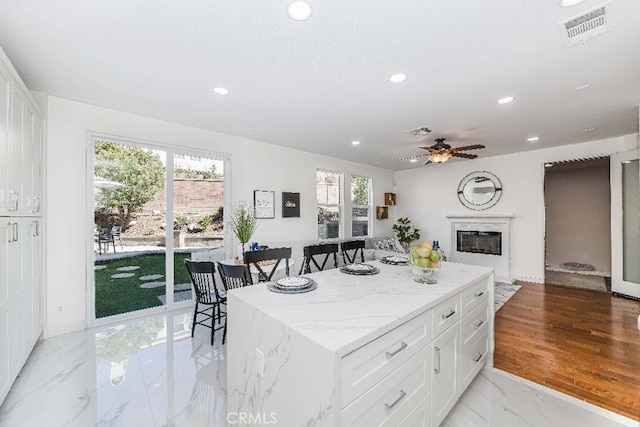 kitchen with white cabinets, ceiling fan, a kitchen island, and light stone countertops