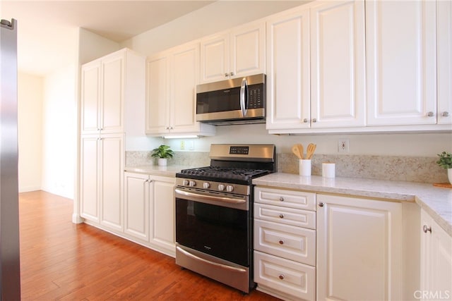 kitchen with white cabinets, appliances with stainless steel finishes, hardwood / wood-style flooring, and light stone countertops