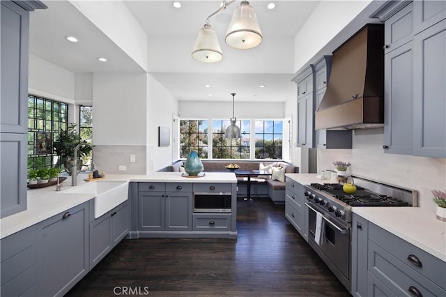 kitchen with wall chimney range hood, dark wood finished floors, a peninsula, stainless steel appliances, and a sink