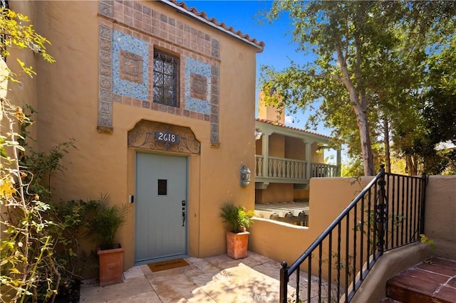 doorway to property with elevator, stucco siding, a tiled roof, and a balcony