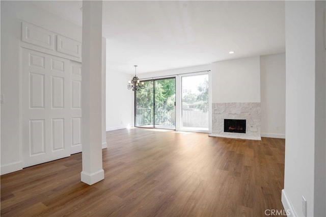 unfurnished living room with hardwood / wood-style flooring, a stone fireplace, and a chandelier