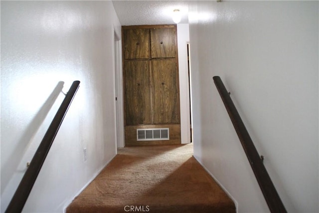 stairs with carpet floors and a textured ceiling